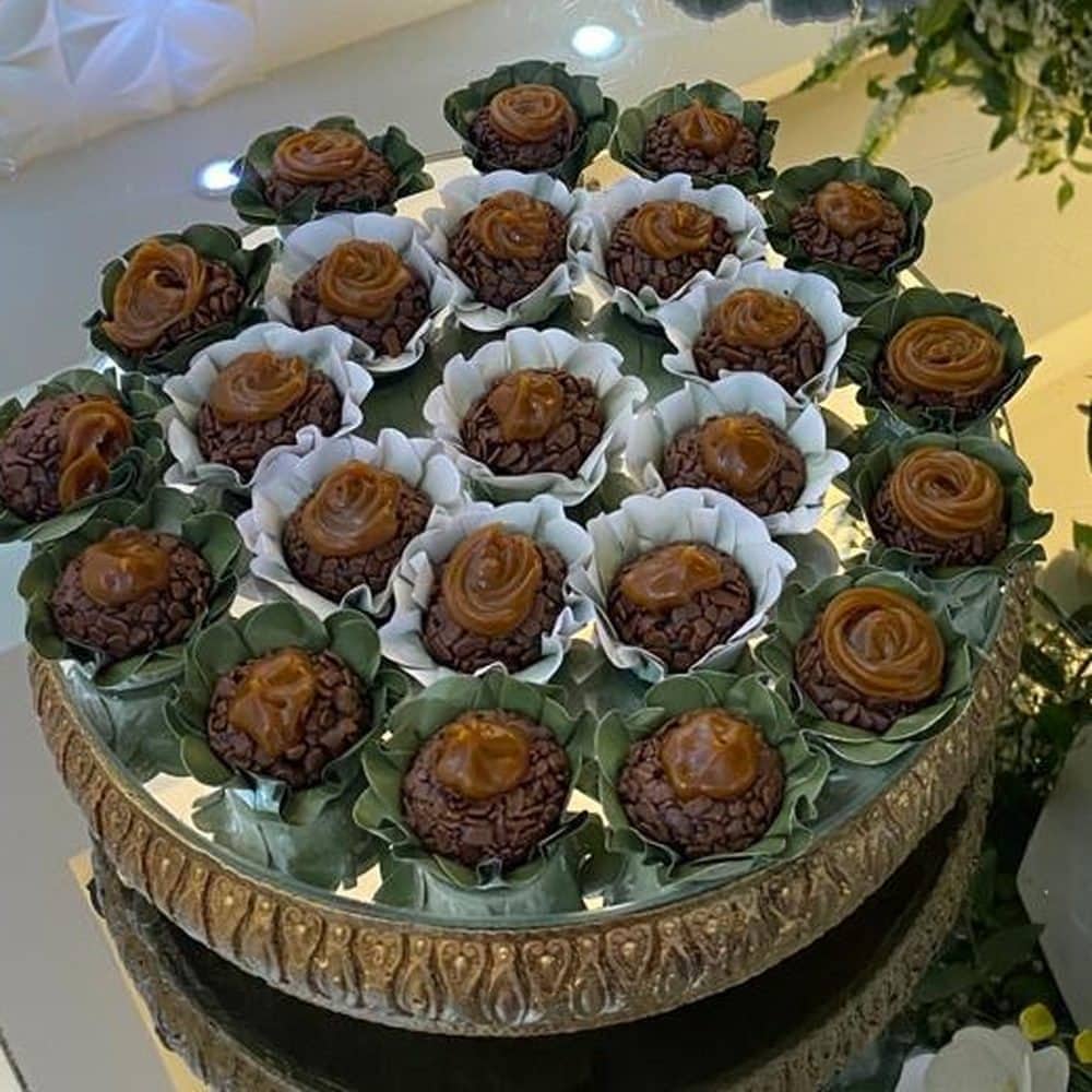 Brigadeiros em forminhas dispostos sobre bandeja dourada, entre folhagens